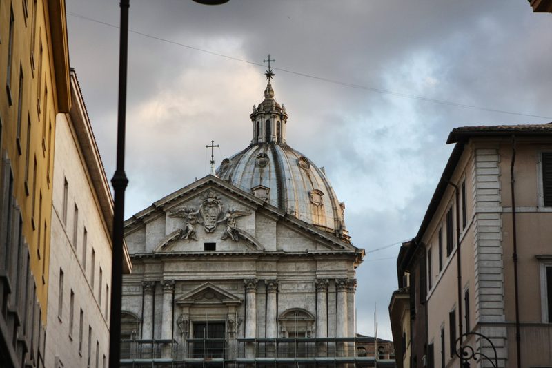 A church dome framed between two buildings under a cloudy sky.