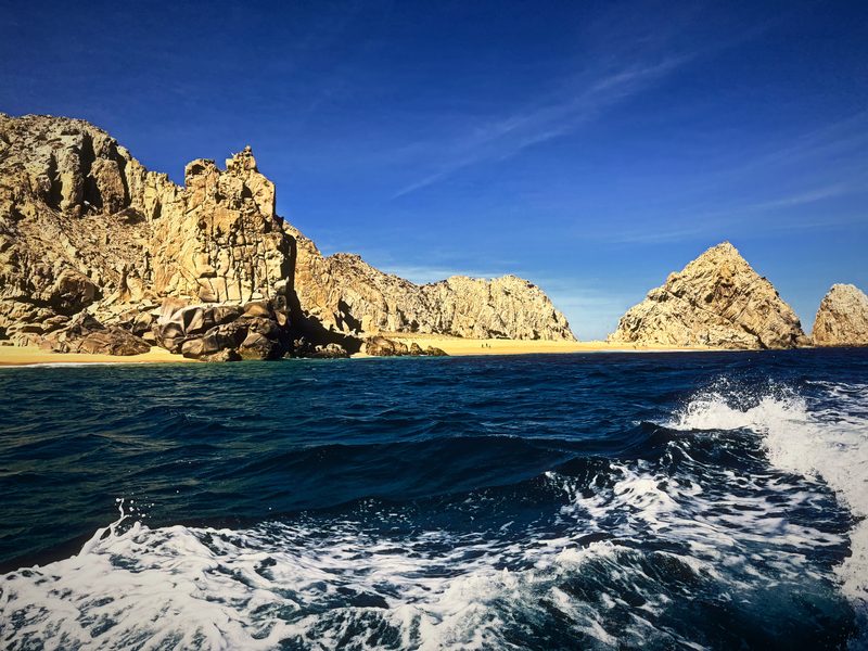 Churned white wake leading across blue water toward tall sea stacks.