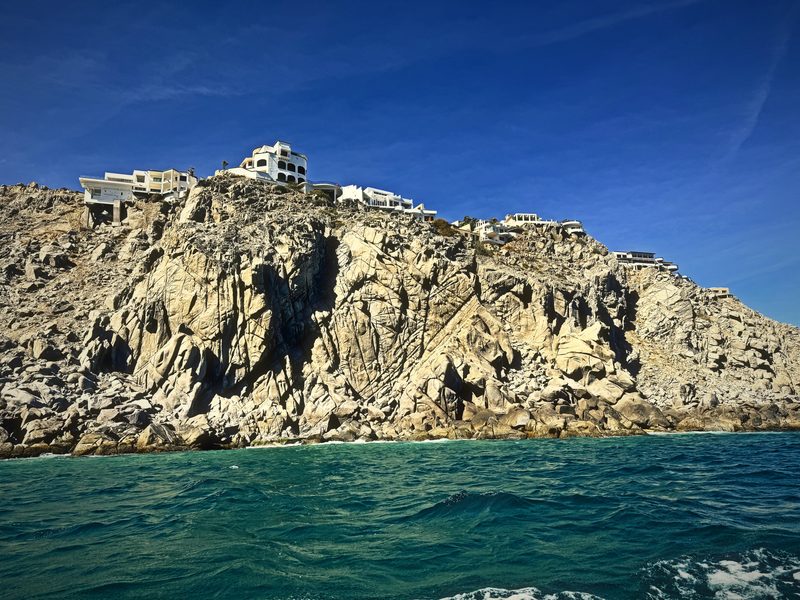 A long granite headland with white buildings perched along its ridge above green water.