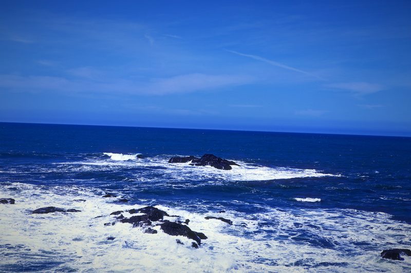 White foam swirling among dark jagged rocks under a blue sky.
