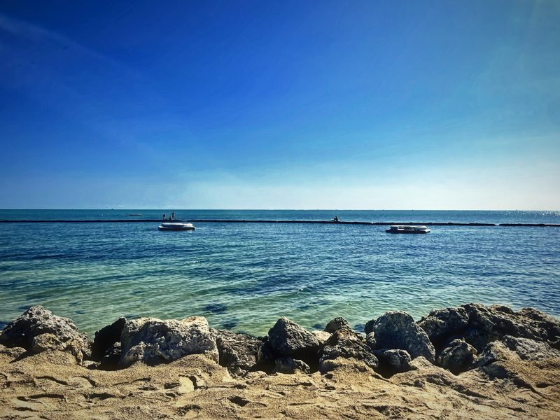 A line of rough boulders in front of calm turquoise water and a pale horizon.