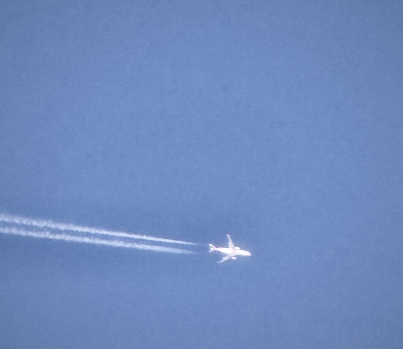 A jet trailing a long white contrail across a deep blue sky.