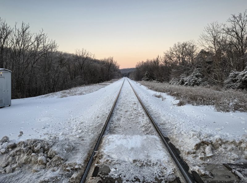 Railroad tracks running straight through fresh snow toward bare winter trees.