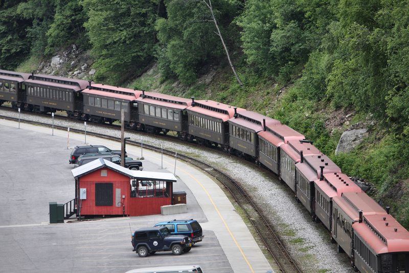 A long line of vintage passenger cars with rose-red roofs curving along a mountainside track.