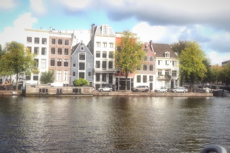 A row of pale canal houses beside a wide river under soft cloud.