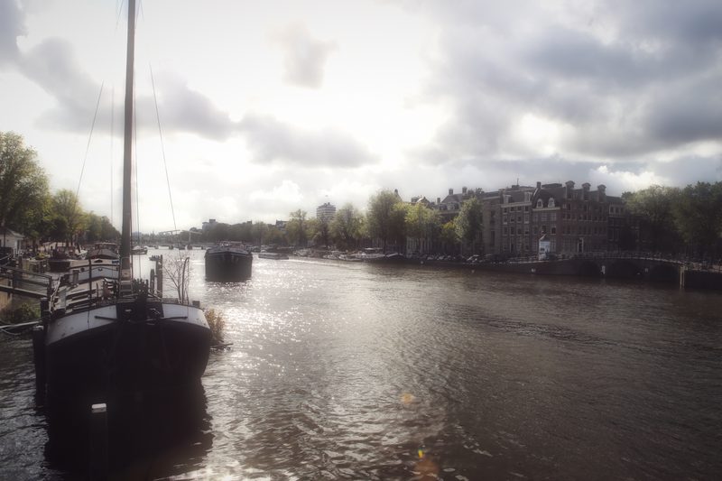 A moored sailing barge with a tall mast on wide grey water under cloud.