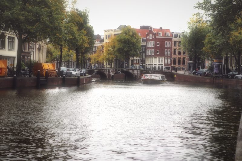 Sunlight glaring off a canal toward bridges and gabled houses.