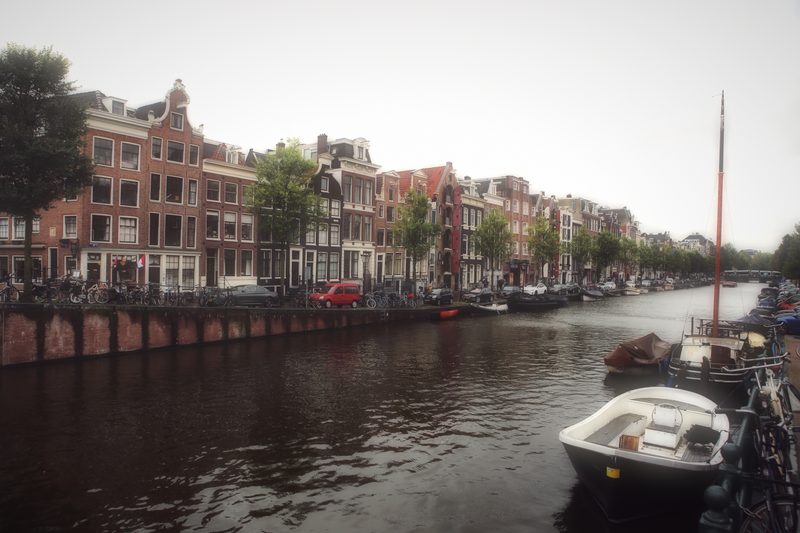 Brick canal houses and a moored boat across hazy water.