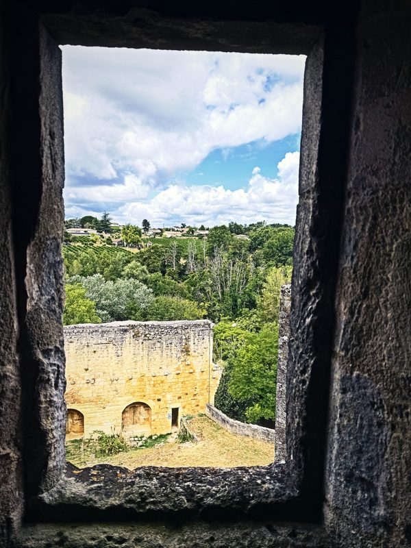 A deep stone window opening framing a view of green woods and a ruined wall below.
