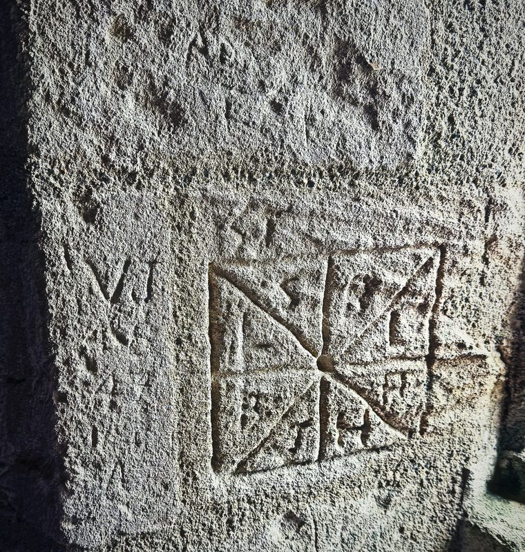 A geometric pattern scratched into pale limestone inside a castle tower.