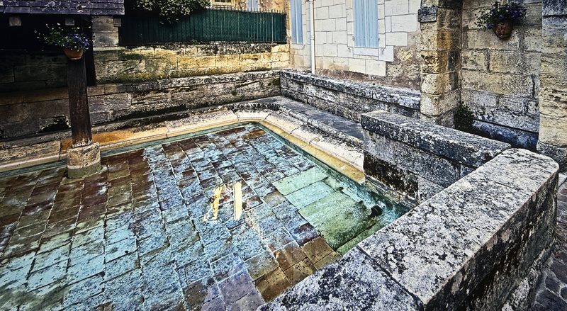 An old stone washing basin filled with clear water reflecting sky and stone.
