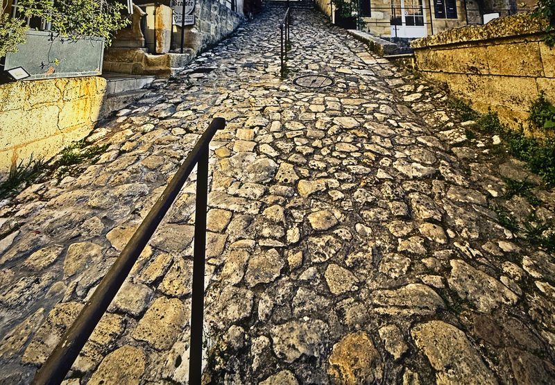 A steep cobbled lane with an iron handrail running down through old stone houses.