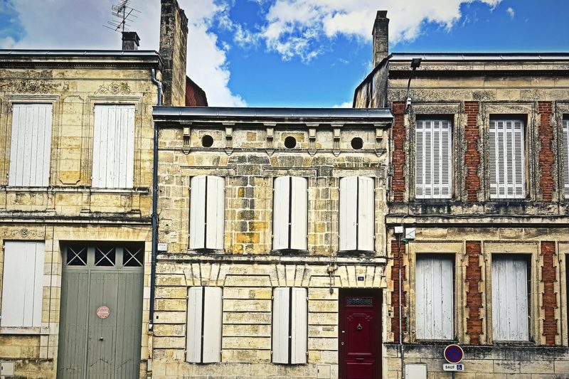Three stone townhouse fronts side by side with pale shutters, a grey garage door and a red door.