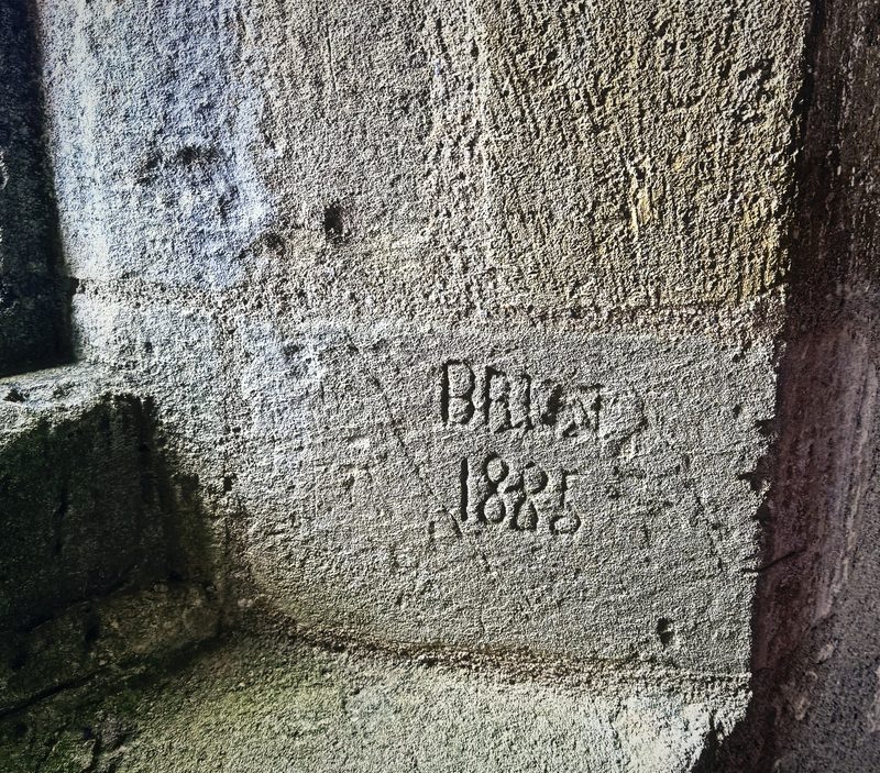 A name and date scratched into a limestone window seat inside a castle tower.