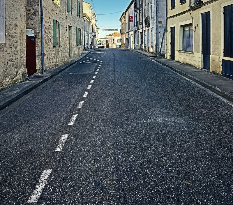 A dashed white centre line running down an empty village street between stone house fronts.