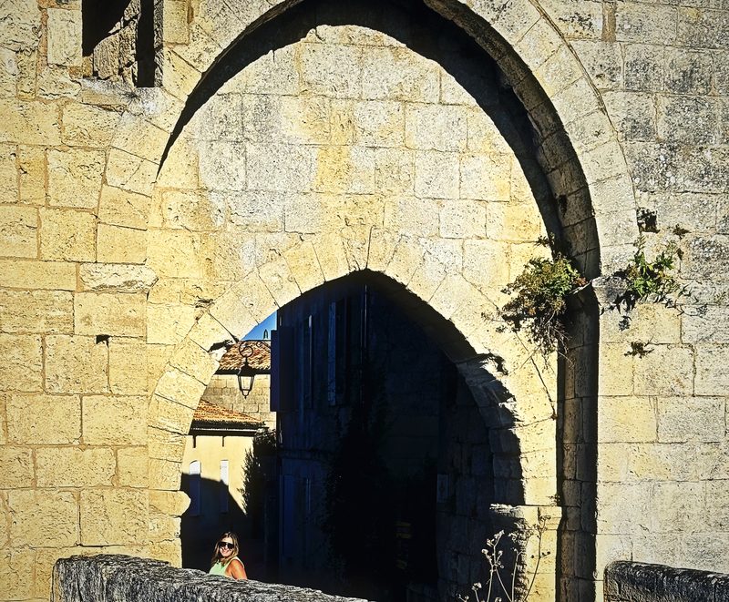 A tall pointed stone arch in sunlit limestone above a shadowed passage and a low wall.