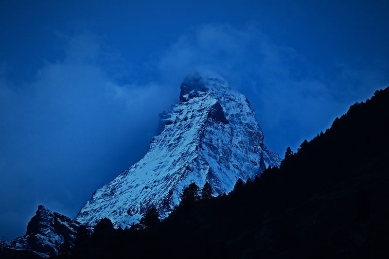 The Matterhorn in deep blue twilight between dark ridges and drifting cloud.