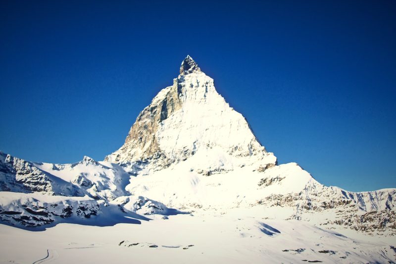 Snowy Matterhorn pyramid rising over a white glacier plateau under a deep blue sky.