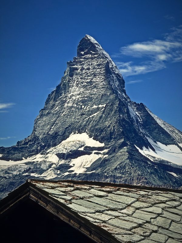 The Matterhorn rising behind a stone-shingled roof under a deep blue sky.