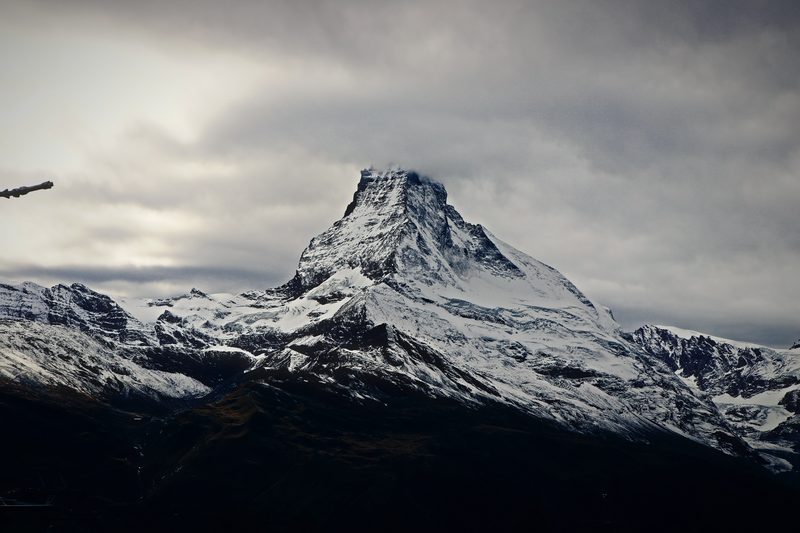 The Matterhorn under a heavy grey overcast with snowy ridges below.