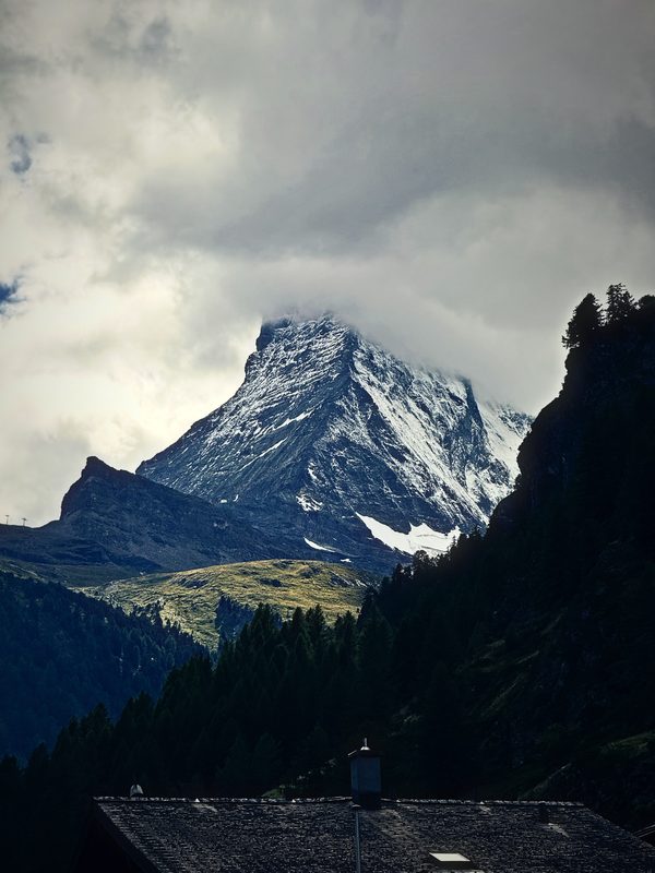 The Matterhorn partly hidden by cloud above dark fir trees.