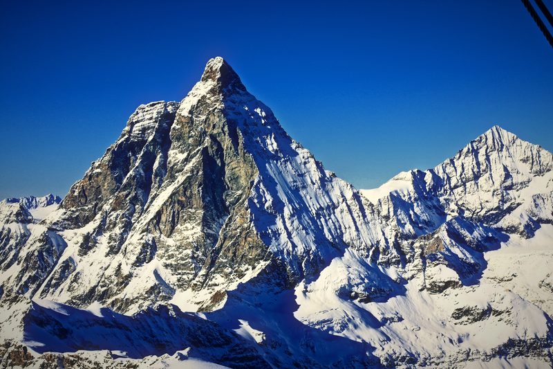 A row of jagged snowy peaks under a dark blue sky.