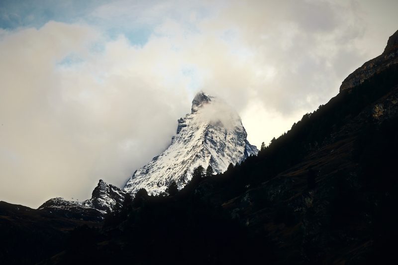 The Matterhorn's summit surfacing through glowing cream cloud above a dark ridge.