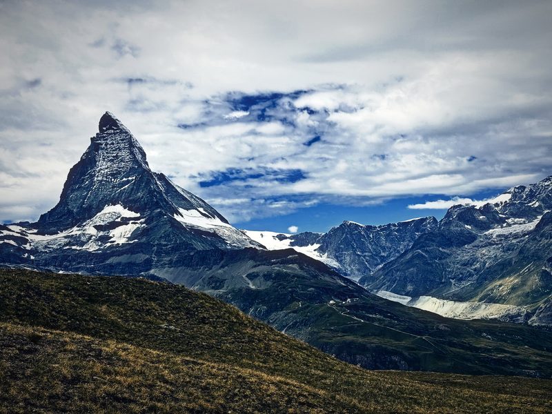 The Matterhorn over a brown alpine meadow under blue sky and cloud.