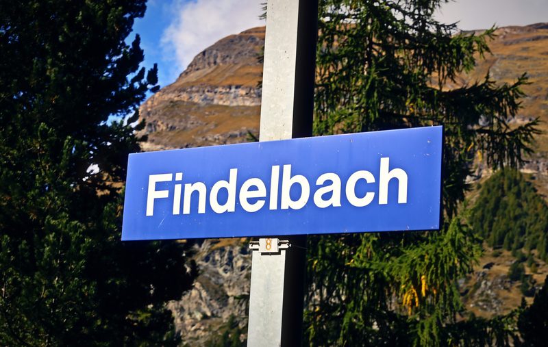 Blue station name board reading Findelbach against pines and a rocky peak.