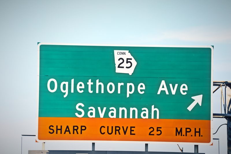 Green highway sign for Oglethorpe Ave, Savannah with an orange sharp curve 25 MPH band.