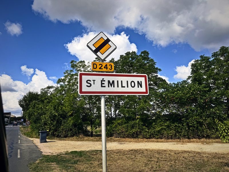 French town entry sign reading St Émilion with D243 and a priority road sign under a cloudy sky.