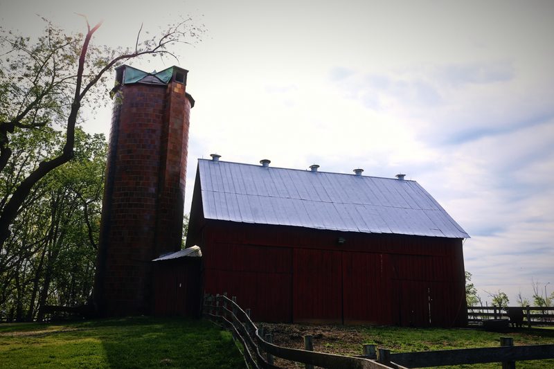 A red barn with a white roof beside a tall brick silo under a pale sky.