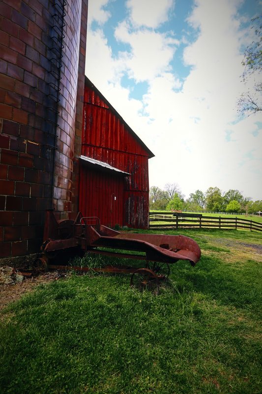 A tight view of a red barn corner rising into a bright cloudy sky over green grass.