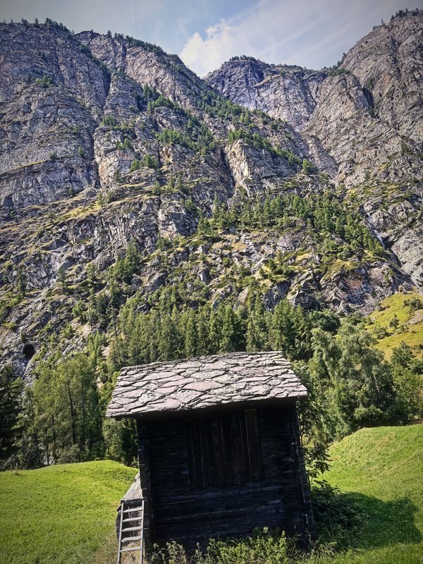 A small dark wooden storage hut with a stone roof below towering rock walls.