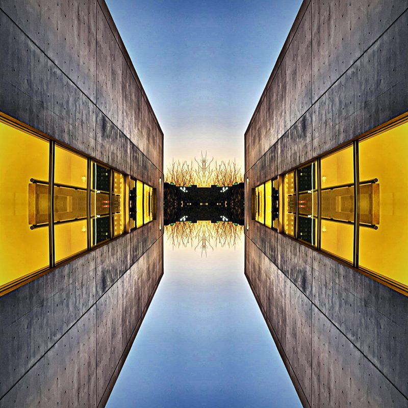 Symmetrical corridor of gold and glass mirrored over still blue water.