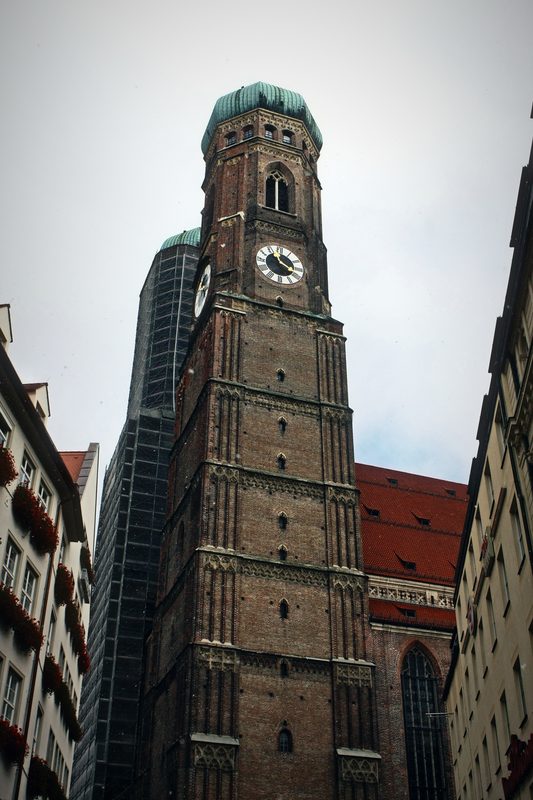 Brick church tower with a clock and green domed top above a narrow street.