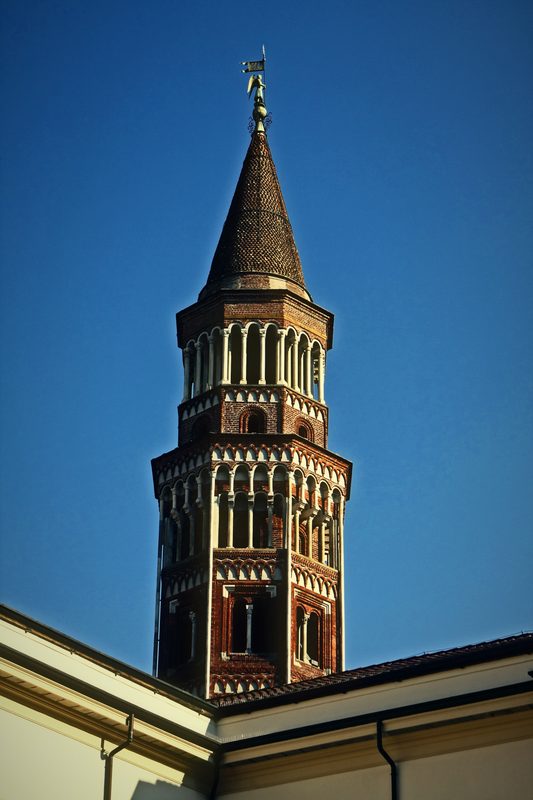 Brick and stone bell tower with a conical top under a clear blue sky.