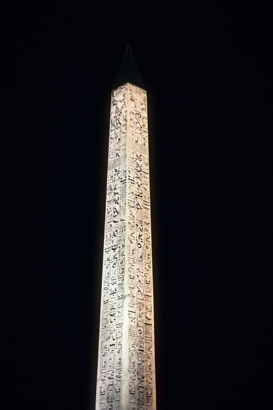 Carved stone obelisk glowing against a black night sky.