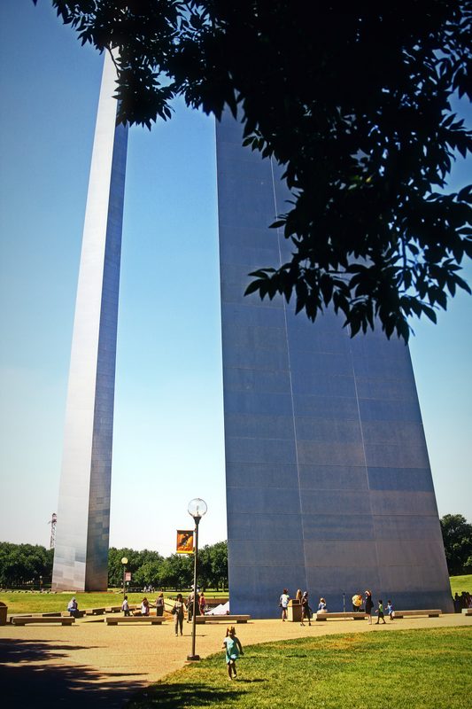 Stainless steel legs of the Gateway Arch rising under summer leaves.