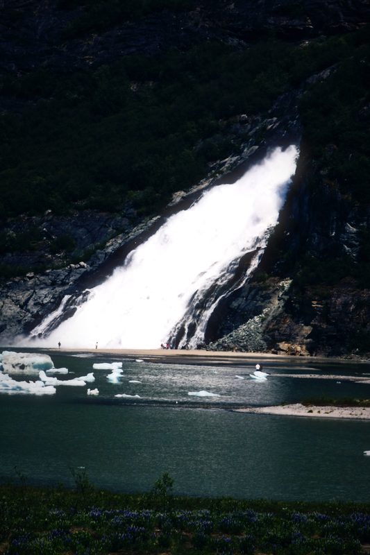A wide waterfall slanting down a dark rock face into still water.