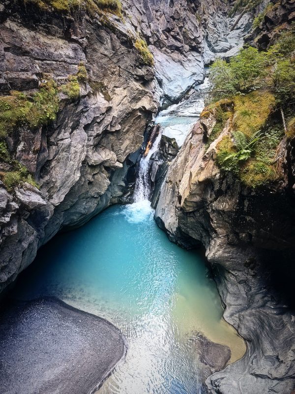 A narrow rock gorge opening onto a bright turquoise pool fed by a small fall.