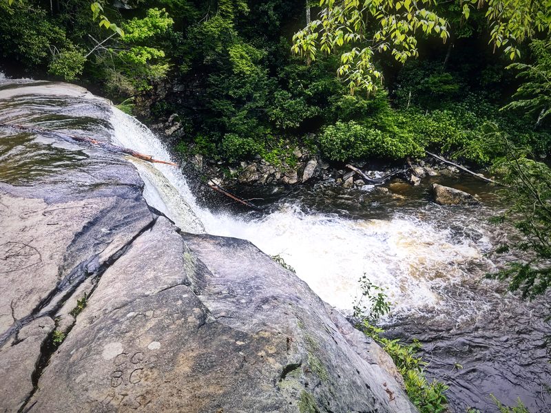 White water sliding over a smooth curved slab of rock into the forest.