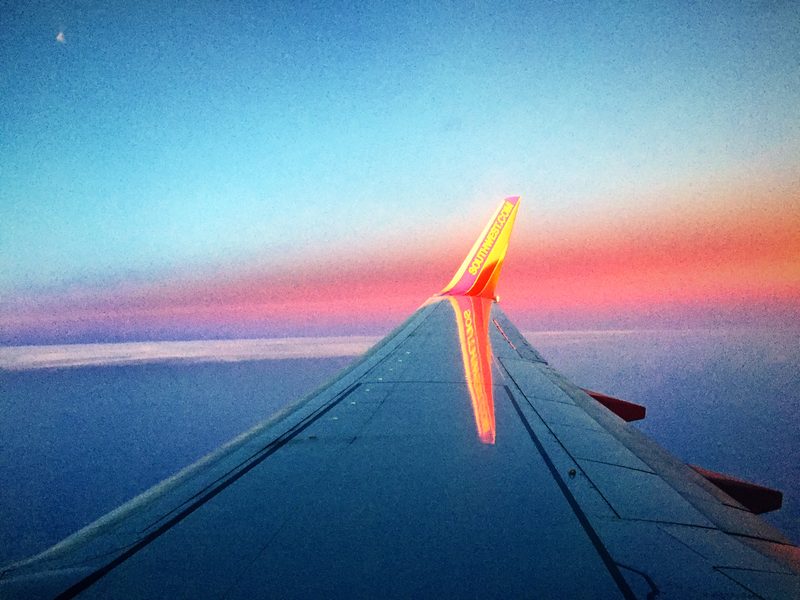 Airplane wing pointing toward a band of pink sunset along the horizon.