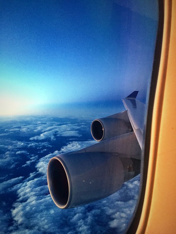 Two jet engines on a wide wing above an ocean of white cloud, seen past the window frame.