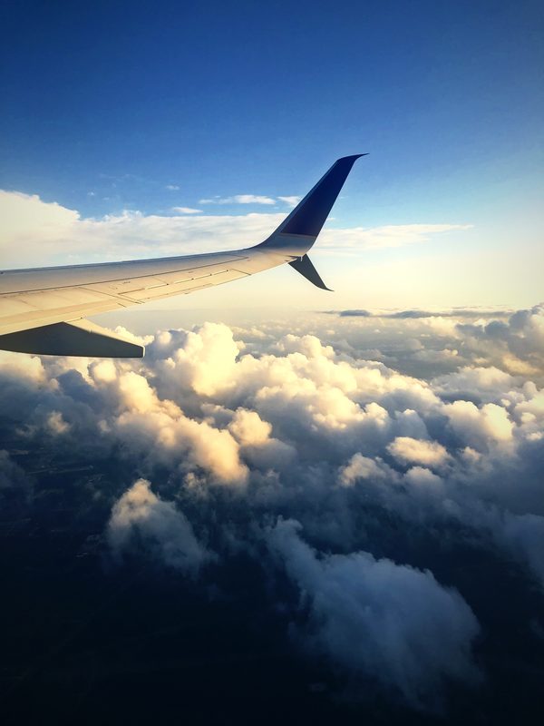 Airplane wing above billowing evening clouds lit by low sun.