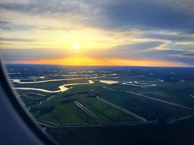 Winding river and wetlands seen from the air with the sun setting on the horizon.