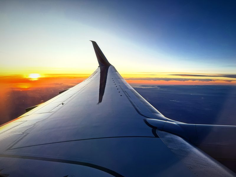 Airplane wing turning silver as the sun sets into a band of orange over the desert.