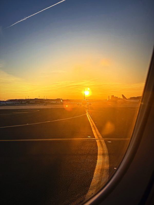 Sun setting over an airfield, with a curving taxiway line seen through the window.