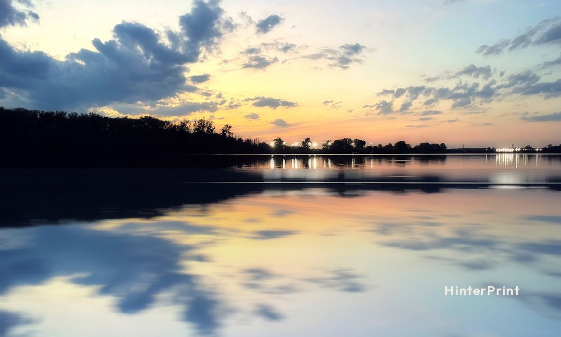 Front of the tag: clouds and a tree-lined shore at dusk, mirrored in the water, with a small HinterPrint mark.